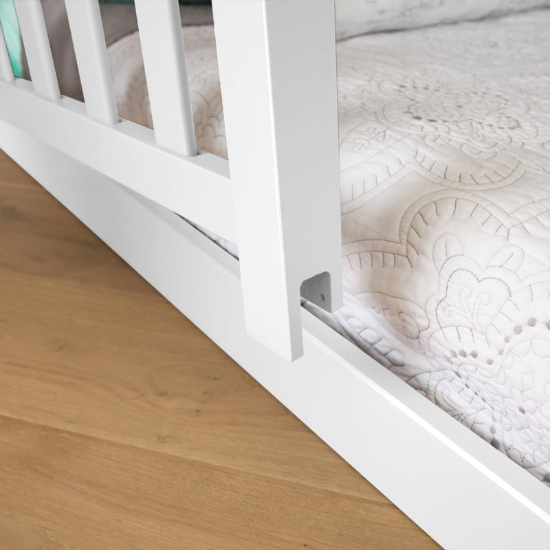 Close-up of white wooden bed frame rail and slats on hardwood floor with decorative quilted white mattress cover