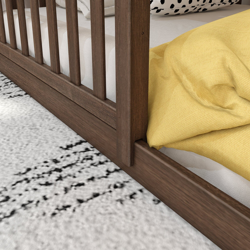 Close-up of a walnut wooden bed frame with vertical slats, textured white mattress, yellow duvet and black-and-white patterned pillow on a speckled area rug in a modern bedroom