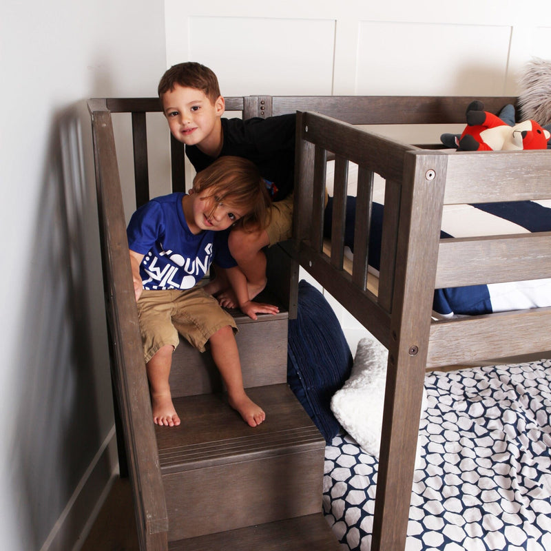 Two smiling boys sitting on wooden bunk bed stairs in a modern kids' bedroom with navy-and-white bedding, cozy pillows, and a stuffed fox toy