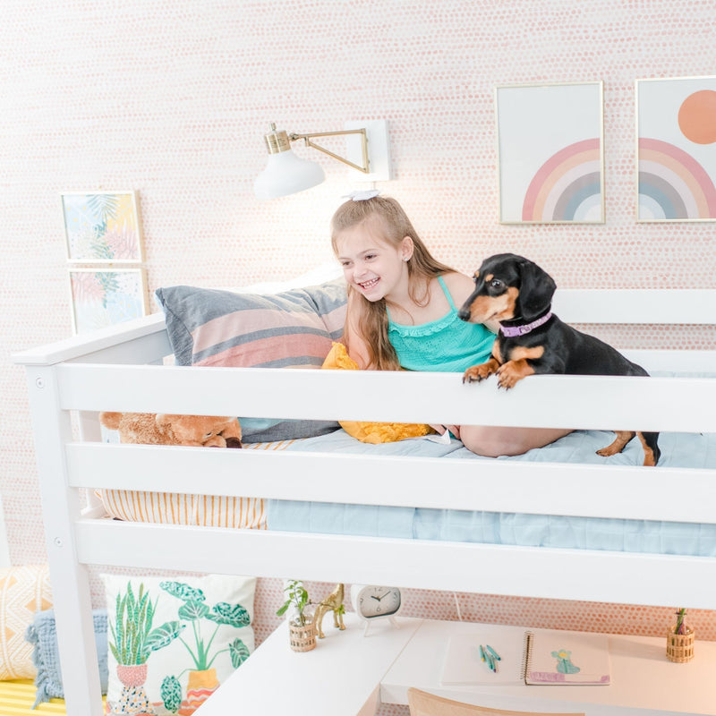 Smiling girl and black-and-tan dachshund on a white bunk bed in a pastel kids bedroom with rainbow wall art, cozy striped bedding and built-in study desk