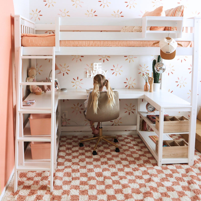 Peach and white kids loft bed with built-in study desk and coral bedding, child seated at desk in sun-pattern wallpapered study nook with cactus and playful bedroom decor