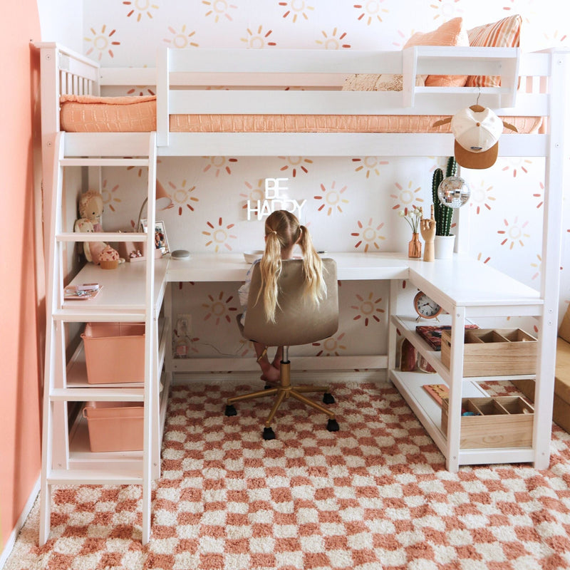 Peach and white kids loft bed with built-in study desk and coral bedding, child seated at desk in sun-pattern wallpapered study nook with cactus and playful bedroom decor