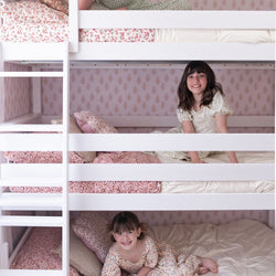 Kids enjoying a triple bunk bed with decorative pillows in a cozy bedroom.