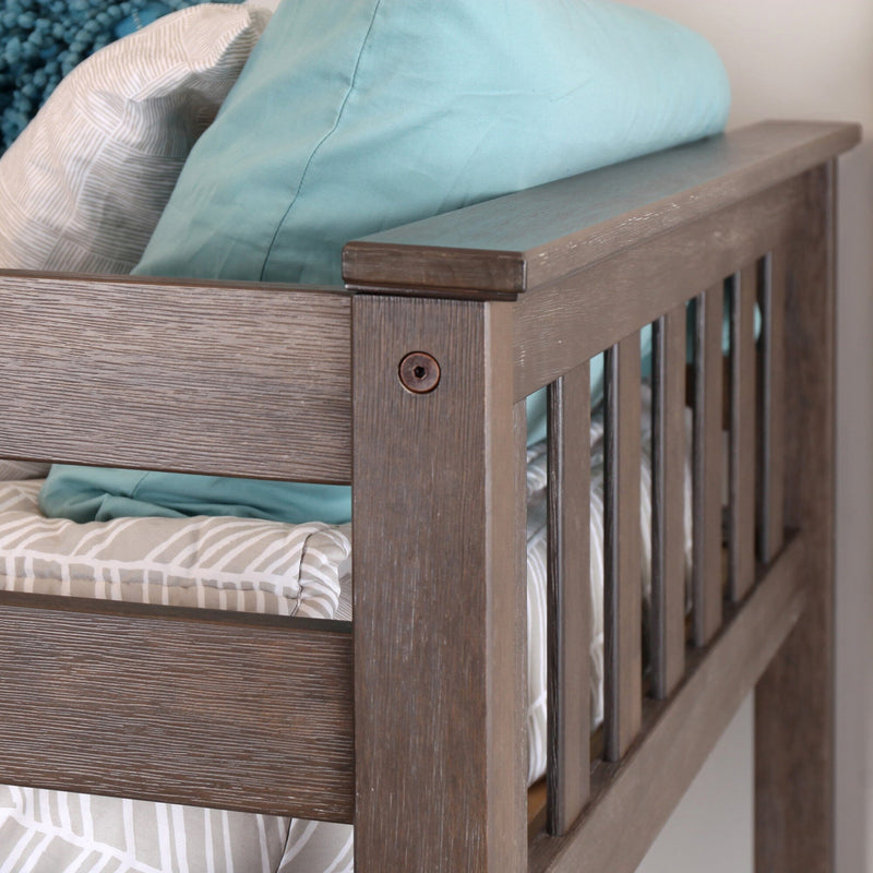 Close-up of gray wooden crib railing and slatted side with teal pillow and gray-and-white patterned crib bumper in a nursery