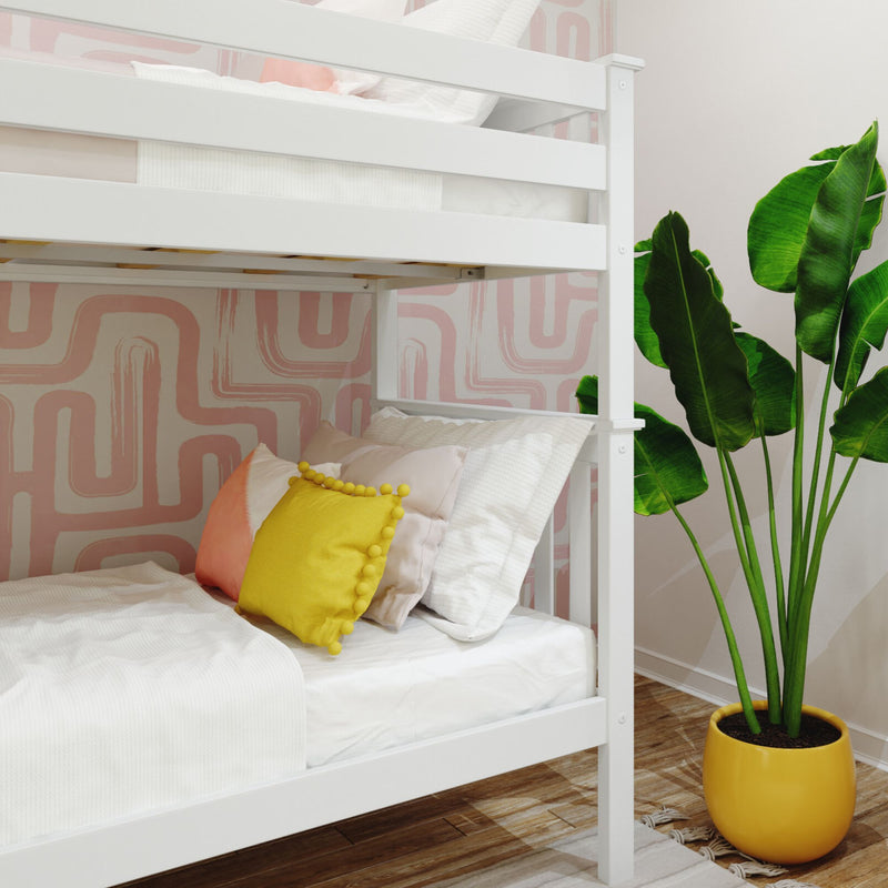 White wooden bunk bed in a children's bedroom with pink abstract geometric wallpaper, white bedding, yellow pom‑pom accent pillow and coral throw pillow, hardwood floor and large potted bird of paradise plant in a yellow planter