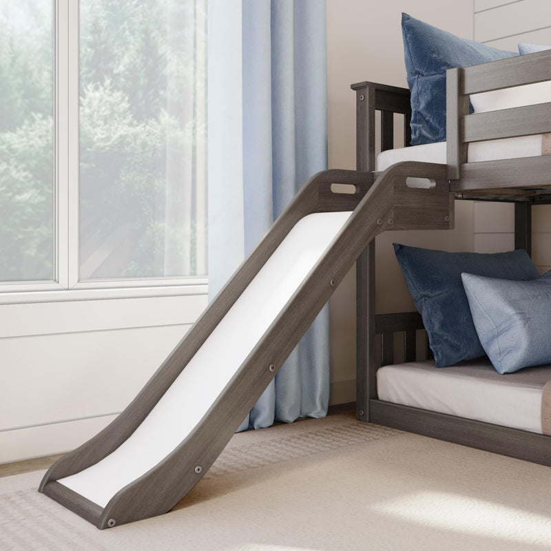 Gray wooden children's loft bunk bed with attached white slide, blue pillows and neutral rug in a bright modern kids' bedroom by a window