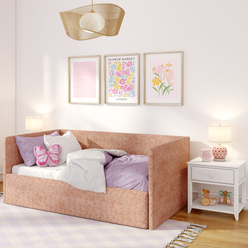 Cozy pastel pink children’s bedroom with upholstered daybed, butterfly pillow, floral wall art, woven pendant light and white nightstand with pink alarm clock