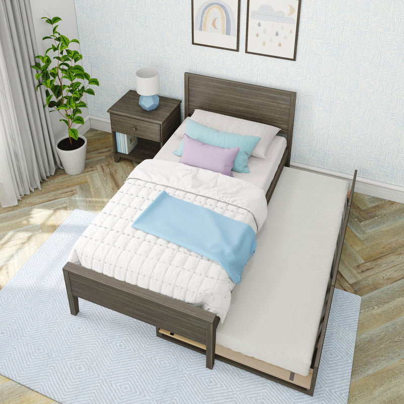 Modern wooden twin bed with pull-out trundle, pastel blue and lavender bedding, wood nightstand with blue geometric lamp, potted plant and patterned wallpaper in bright kids' bedroom