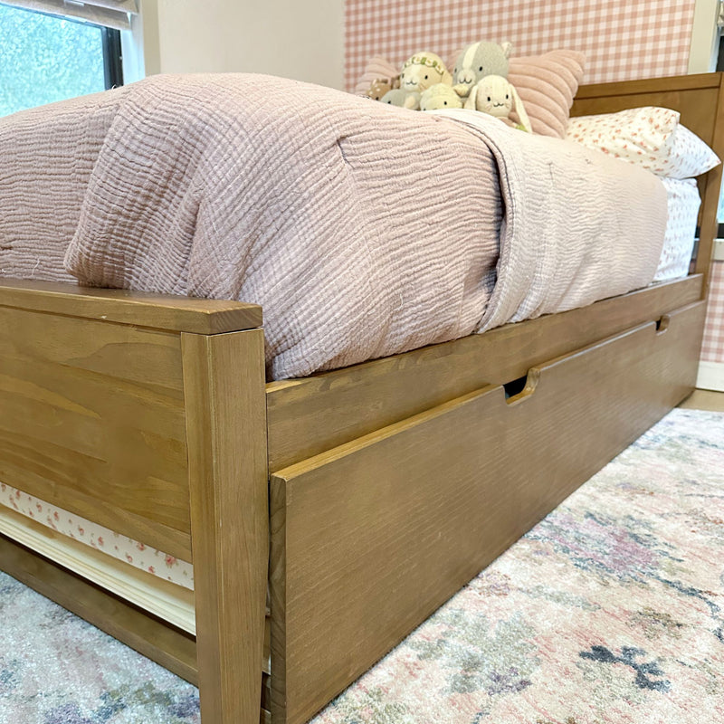 Wooden trundle bed with built-in storage drawers, blush pink quilt, floral sheets and plush stuffed animals in a kids' bedroom