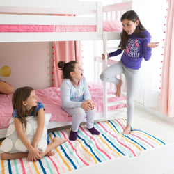 Three children in cozy pajamas enjoying a playful moment near a white bunk bed with pink bedding in a bright, cheerful bedroom with striped rug.