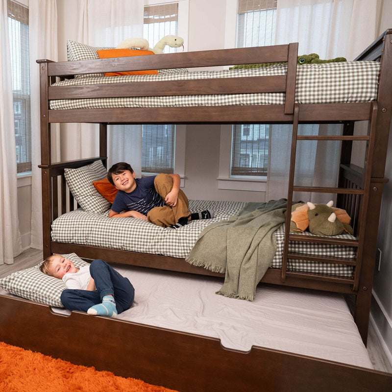 Two smiling boys on a dark wood bunk bed with trundle and ladder, green gingham bedding, orange accent pillows and stuffed animals in a bright kids' bedroom