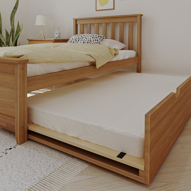 Wooden pull-out trundle bed under a single bed in a bright modern bedroom with yellow blanket, white mattress, bedside lamp and potted plant
