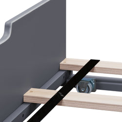Close-up of metal bed frame with wooden slats, caster wheel and black support strap — slatted bed base assembly detail