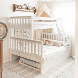 White wooden bunk bed with trundle and ladder in bright neutral kids bedroom with canopy, stuffed animals, floral wall art and cozy bedding