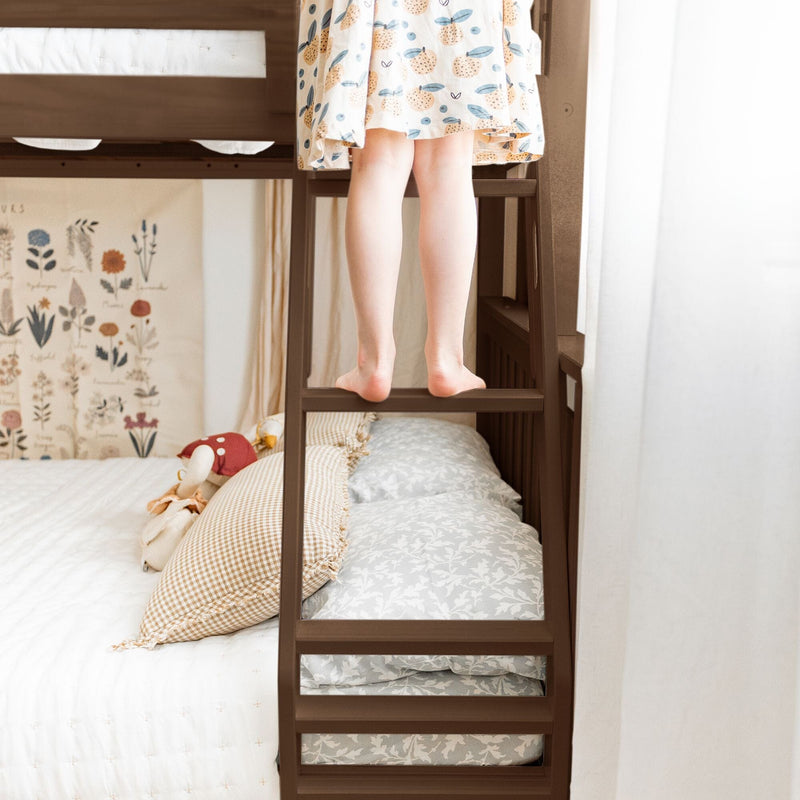 Child standing barefoot on wooden bunk bed ladder in cozy kids bedroom with patterned dress, gingham pillows and botanical wall art