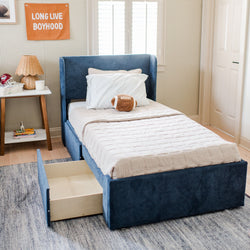 Cozy children's bedroom with a blue velvet twin bed, storage drawer, and football-themed decor.