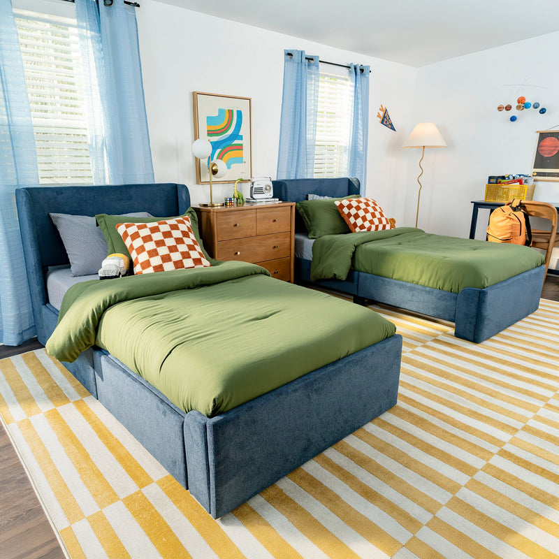 Modern kids twin bedroom with green comforters, blue upholstered beds, checkered pillows, wooden nightstand and yellow striped rug
