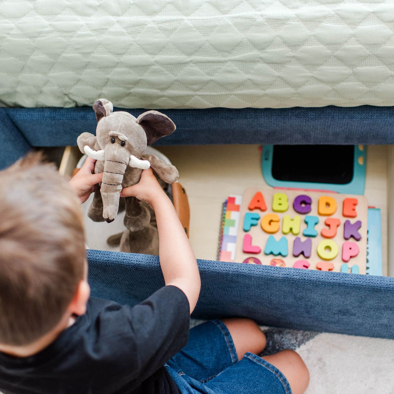 Young child playing with gray plush elephant on bed next to colorful wooden alphabet puzzle — toddler toys, early learning, kids playroom