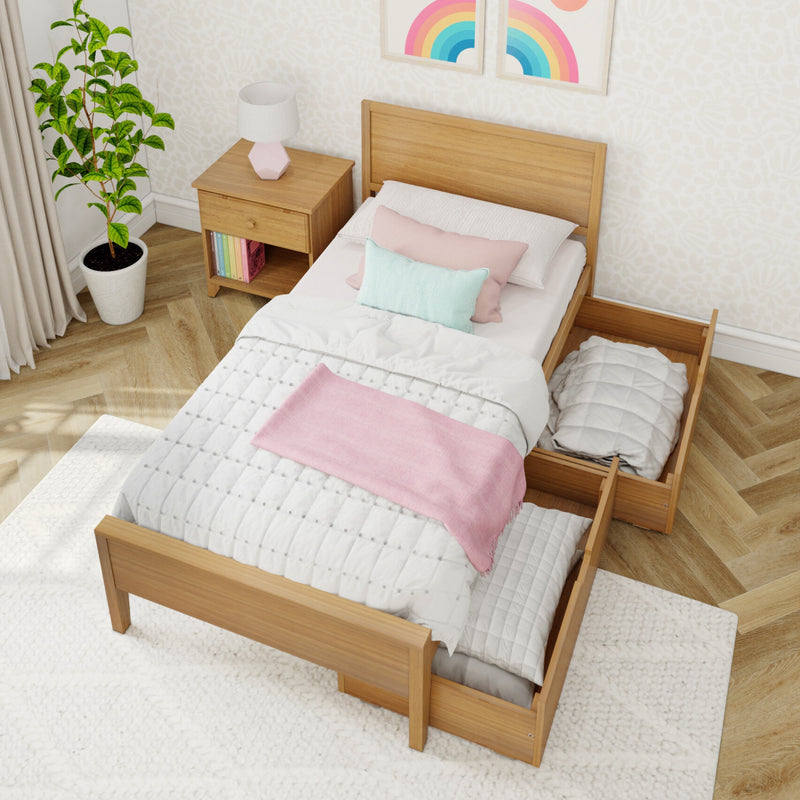 Wooden single bed with pull-out trundle storage, pastel pink and mint bedding, wooden nightstand with lamp, potted plant and rainbow wall art in a bright Scandinavian-style bedroom