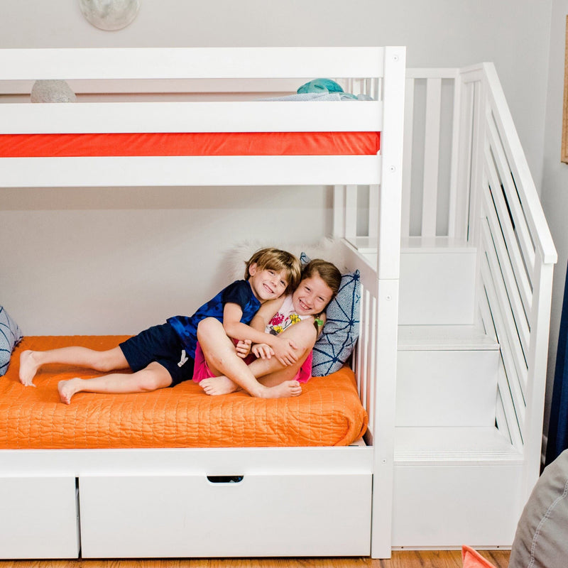 Two children smiling and hugging on an orange-covered lower bunk in a modern white bunk bed with built-in storage stairs in a cozy kids' bedroom