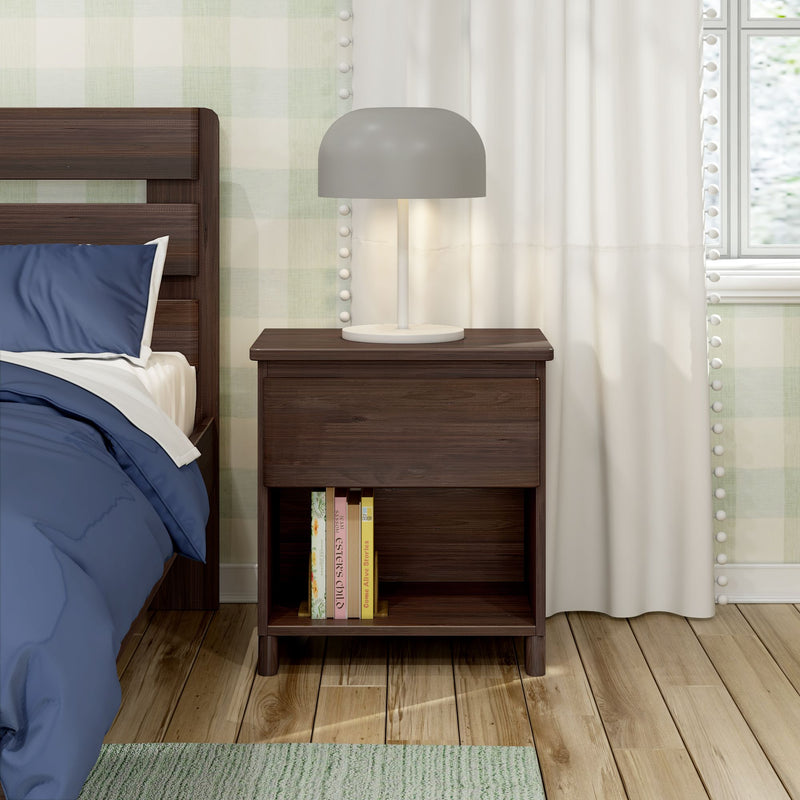 Dark walnut nightstand with gray table lamp and lower shelf of books next to bed with blue bedding on hardwood floor in modern bedroom interior