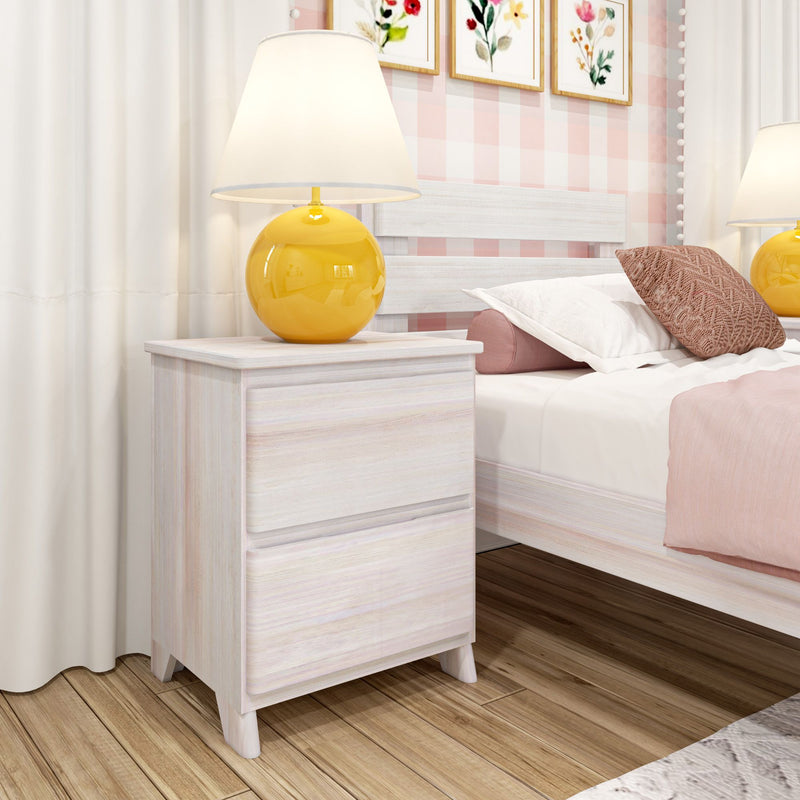 Whitewashed nightstand with yellow ceramic lamp beside bed with pink bedding and decorative pillow, floral wall art and hardwood floor