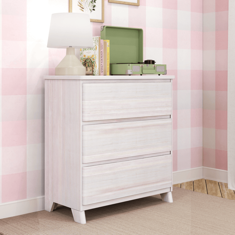 Whitewashed 3-drawer dresser in pink gingham nursery with beige table lamp, children's books and a green portable record player on top