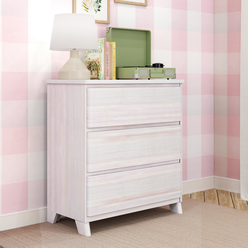 Whitewashed dresser in pink gingham nursery with beige table lamp, green suitcase record player, children's books and framed botanical wall art