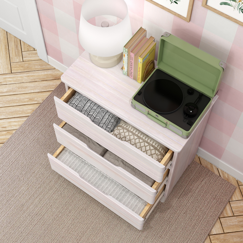 White bedroom dresser with open drawers, folded linens, green portable record player, lamp and books on pink checkered wall