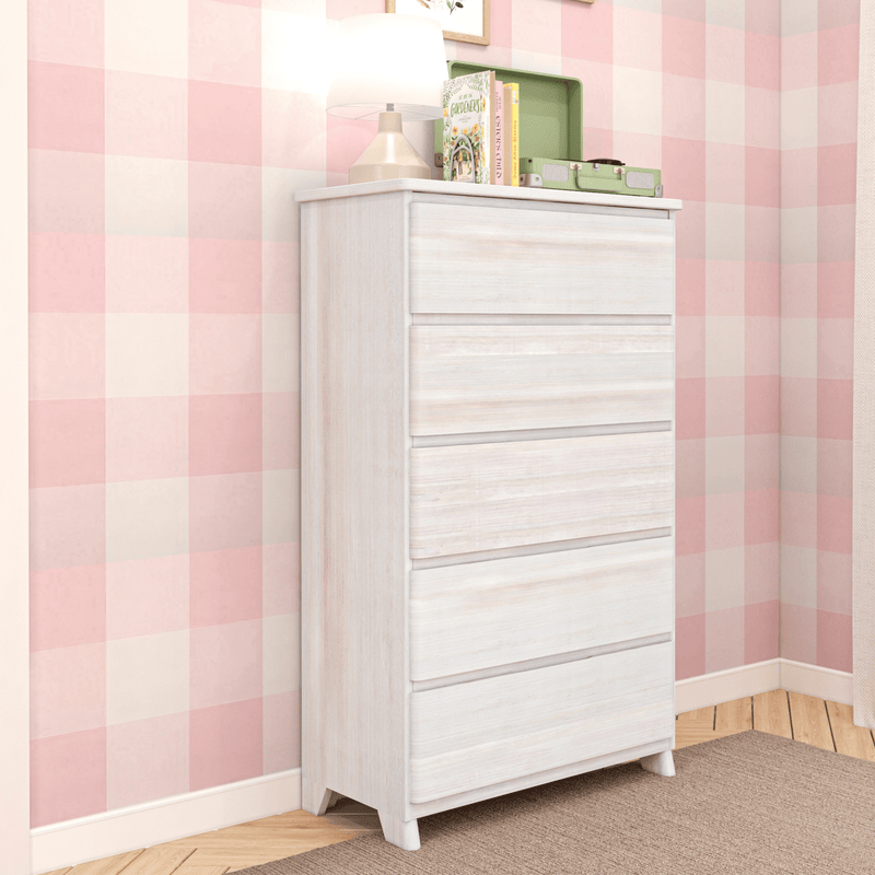White five-drawer wooden dresser in a pink checkered nursery with lamp, children's books and a mint record player on top