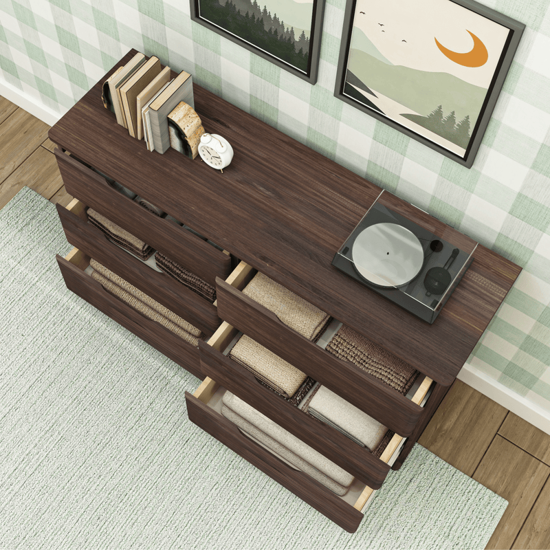 Walnut dresser with open drawers revealing neatly folded blankets, record player, books and alarm clock against green plaid wall – modern bedroom storage solution