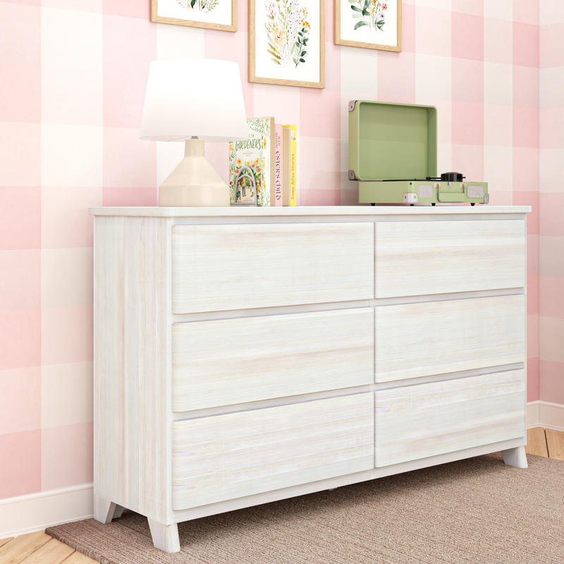 Whitewashed dresser with beige table lamp, books and green vintage record player against pink gingham nursery wallpaper and framed floral prints