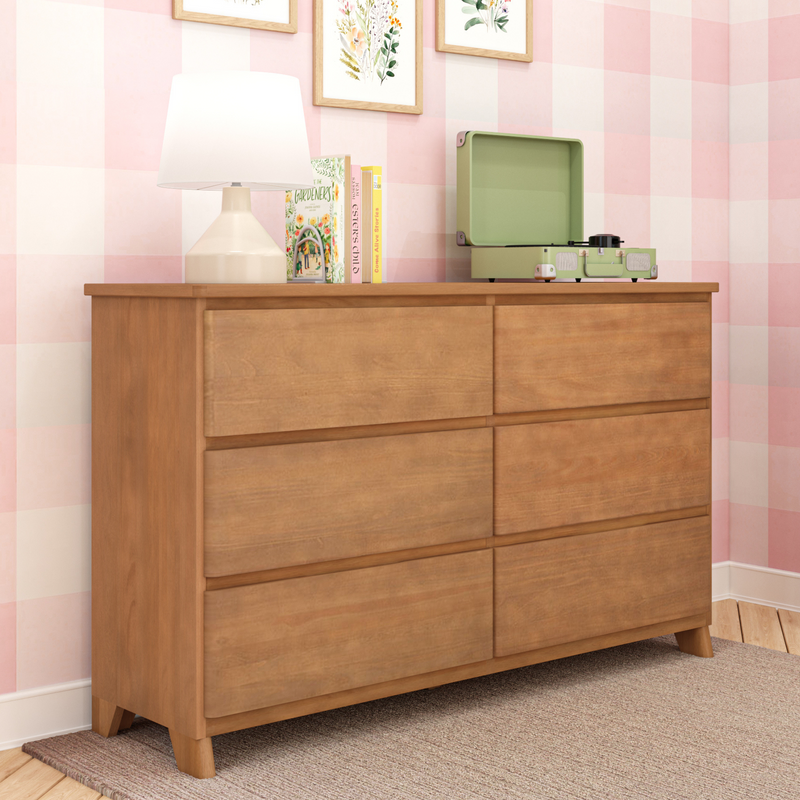 Mid-century wooden dresser in pink gingham nursery with white table lamp, children's books and green portable record player on top