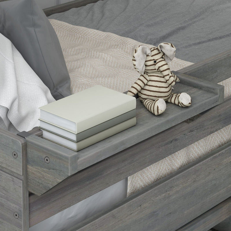 Gray wooden toddler bed with beige knit blanket, stack of books on the bed rail and striped elephant plush toy — neutral nursery decor