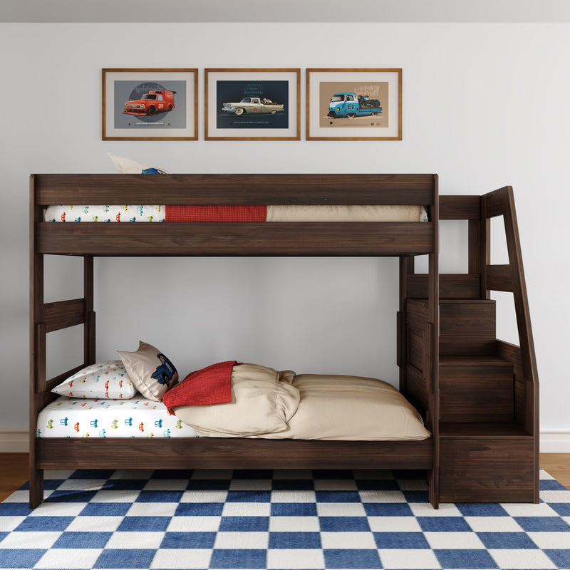Dark wood children's bunk bed with built-in storage stairs, car-print sheets and pillow, beige comforter with red throw, blue checkered rug and three framed vintage car posters on white wall
