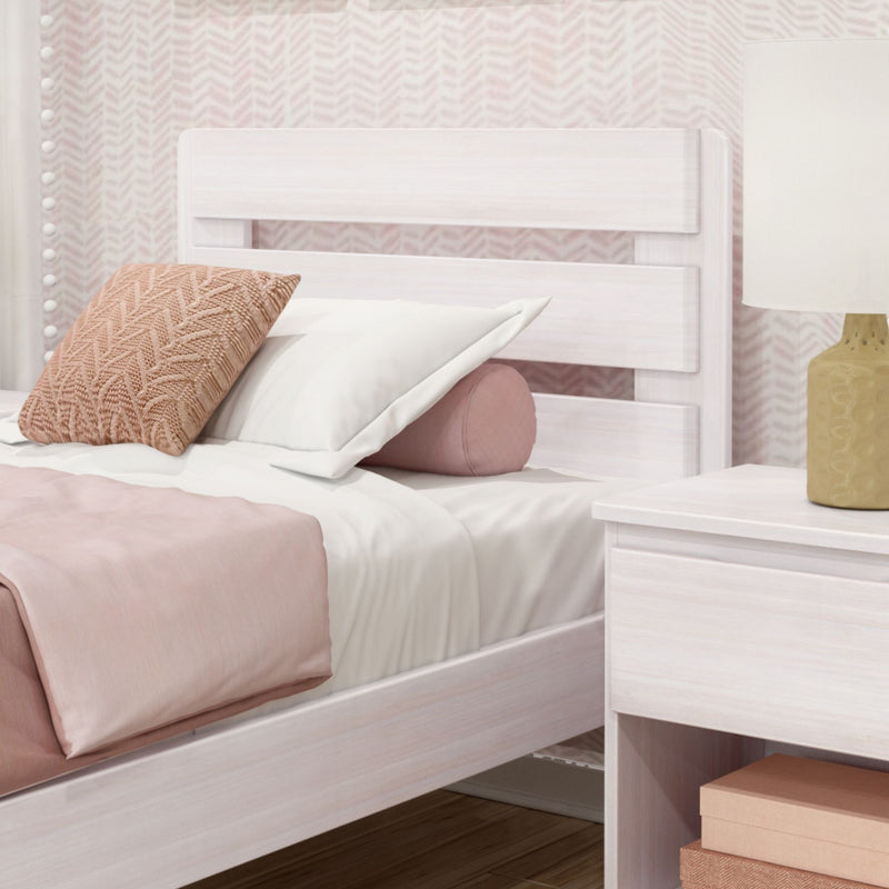 Whitewashed wooden bed with blush pink bedding, textured knit throw pillow and round bolster, white nightstand and beige lamp against chevron pink wallpaper, modern girls bedroom decor