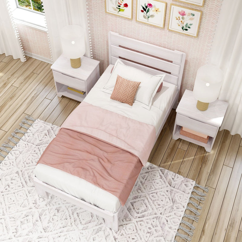 Cozy pastel pink bedroom interior with white wooden twin bed, blush bedding, matching nightstands, gold-base lamps, floral wall art and textured boho rug