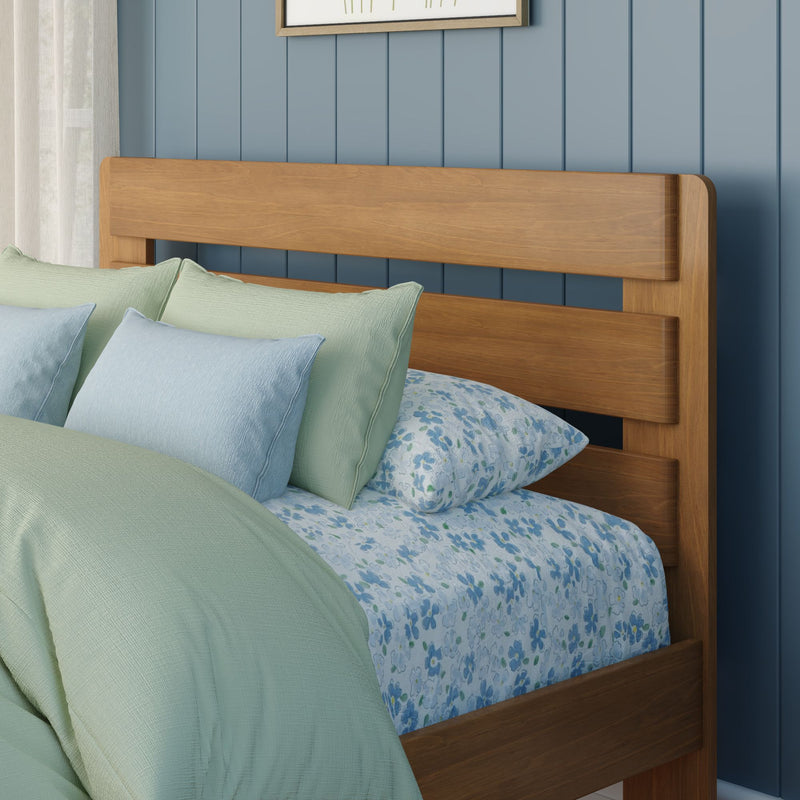 Solid wood headboard against blue paneled wall with pastel green and light blue pillows, floral quilt, cozy bedroom decor