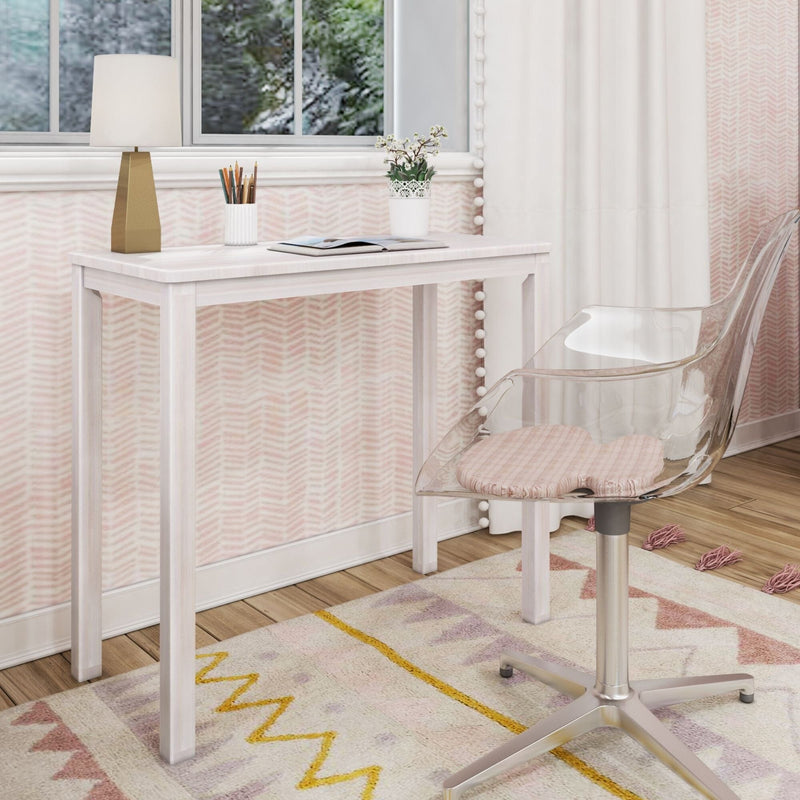 Modern pastel pink girls' bedroom study nook with white wooden desk, gold geometric table lamp, clear acrylic swivel chair, open notebook, pencil holder, potted plant and patterned rug