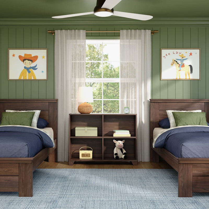Shared kids' bedroom with twin wooden beds, green paneled walls, navy bedding, sheer curtains over a window, woven bedside lamp, ceiling fan, cowboy-themed framed art and plush cow toy