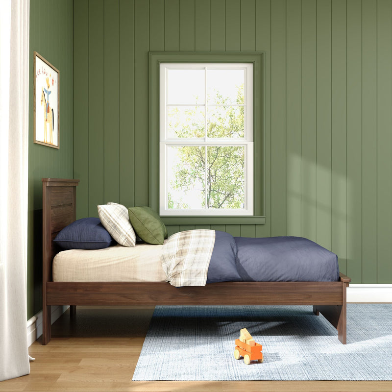 Sunlit green paneled kids' bedroom with wooden twin bed, navy bedding, plaid throw pillows, white-framed window and wooden toy on blue rug
