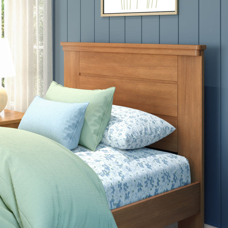 Modern bedroom interior with solid wood bed headboard, mint green quilt, pastel blue pillows and floral blue sheets against a navy shiplap wall and sheer curtains