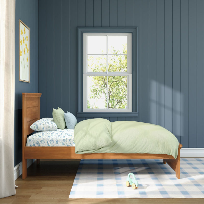 Sunlit children's bedroom with blue paneled walls, wooden single bed with green duvet and floral sheets, window, framed flower art and toy on a checkered rug