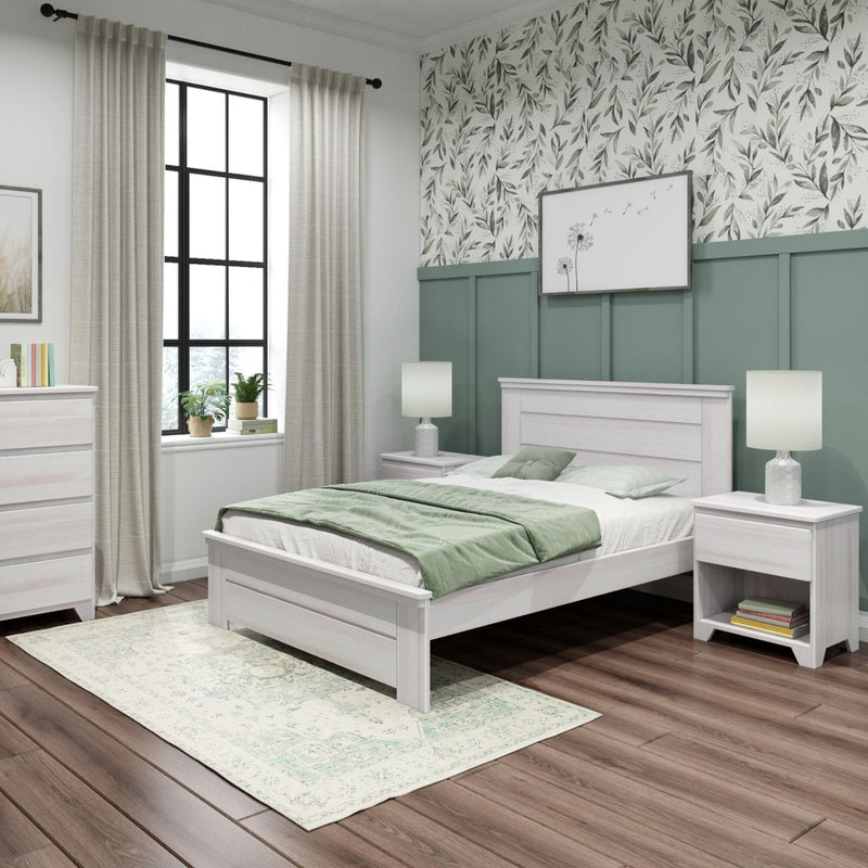 Modern farmhouse bedroom with whitewashed wood bed, sage green bedding, floral wallpaper and board-and-batten wainscoting, matching nightstands with lamps, large black-framed window, dresser, patterned area rug and hardwood floors