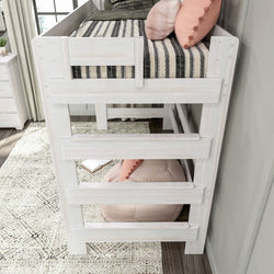 White wooden loft bed with pink and black accents, featuring a cozy pillow and blanket, in a stylish bedroom setting with a neutral rug and natural light.