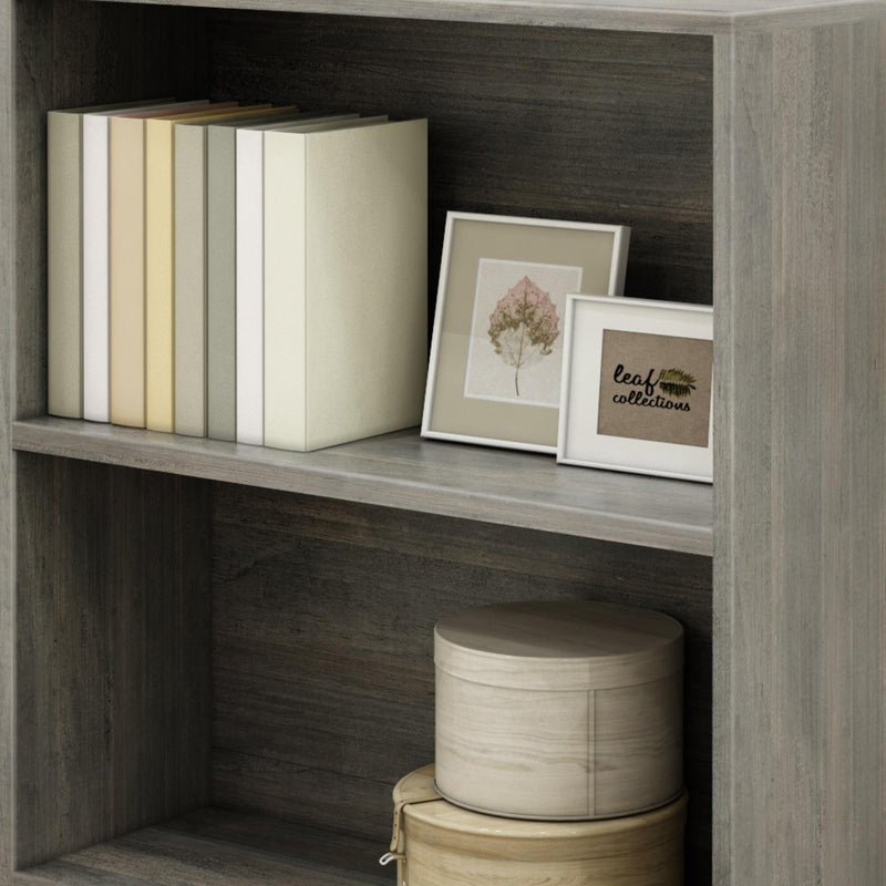 A wooden bookshelf with neatly arranged books, decorative framed pictures, and round storage boxes.