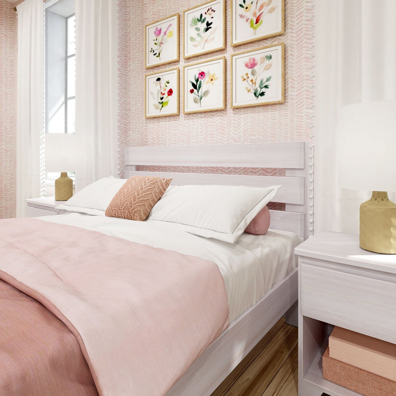 Soft pink modern bedroom with whitewashed wood bed, pastel pink bedding and textured throw pillow, floral framed gallery wall, white curtains and gold bedside lamps