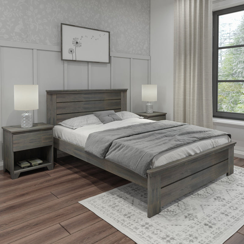 Gray rustic wooden platform bed with slatted headboard, matching nightstands and lamps, white bedding with gray throw, patterned area rug and hardwood floors in a neutral farmhouse bedroom with large window and decorative wall art