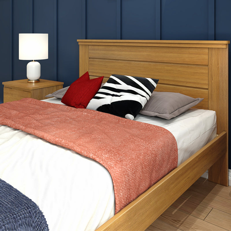 Modern oak bed and headboard by navy paneled wall with white bedside lamp, red and black decorative pillows and coral throw blanket