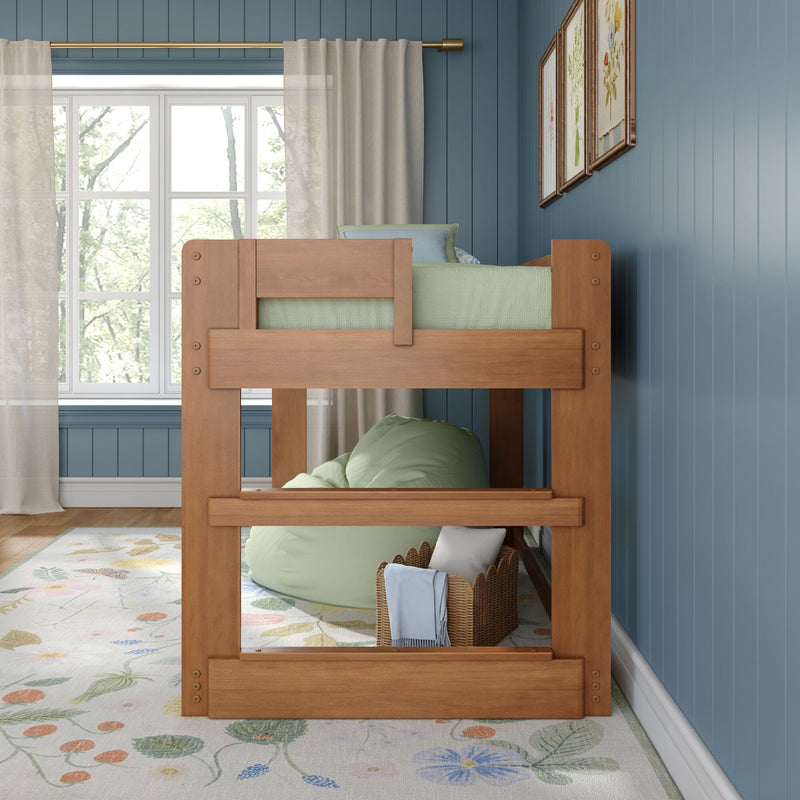 Wooden bunk bed in a cozy blue kids' bedroom with natural light from a paneled window, sheer curtains, floral rug, green bean bag, wicker basket and framed botanical prints.